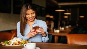 Woman holding a mobile phone and enjoying a breakfast.